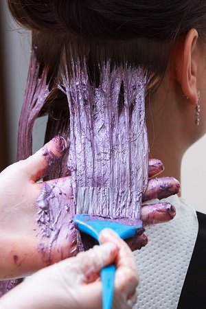 hairdresser applying color female customer at salon, doing hair dye